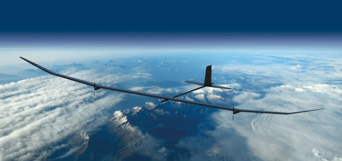 A sleek, elongated drone flies high above a cloud-covered landscape, showcasing its wingspan against a backdrop of blue sky and distant mountains.
