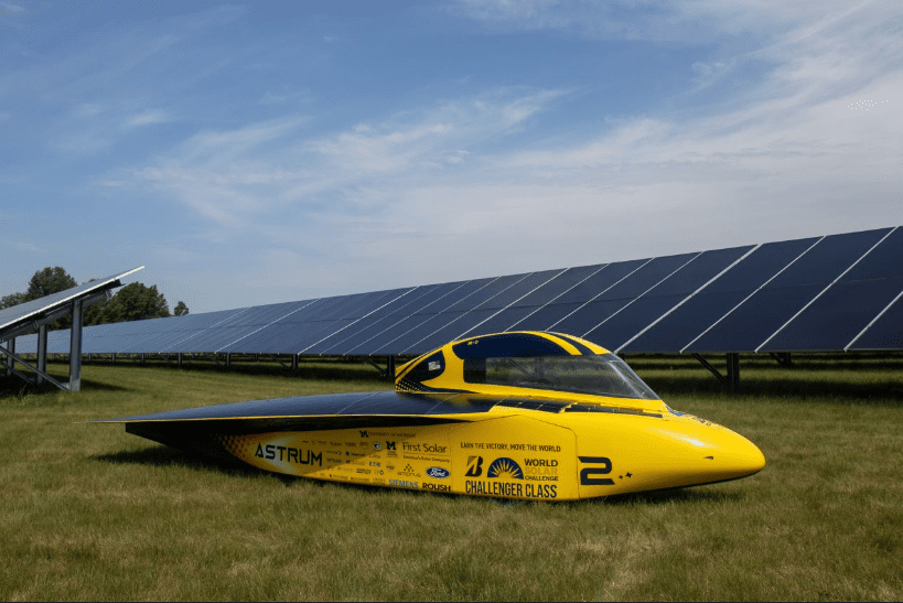 A sleek, yellow solar vehicle is parked amidst solar panels under a blue sky, showcasing innovative green technology.