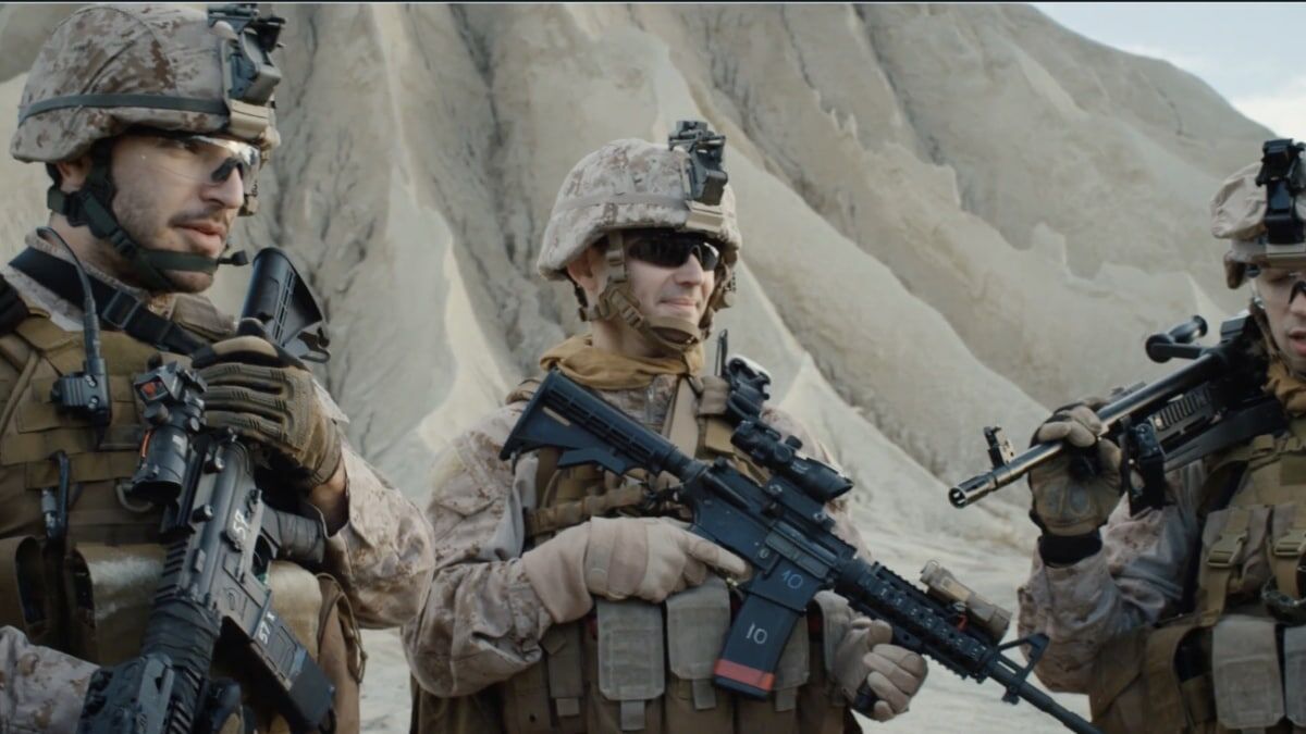 Three soldiers in tactical gear hold weapons while standing against a rugged, sandy landscape.