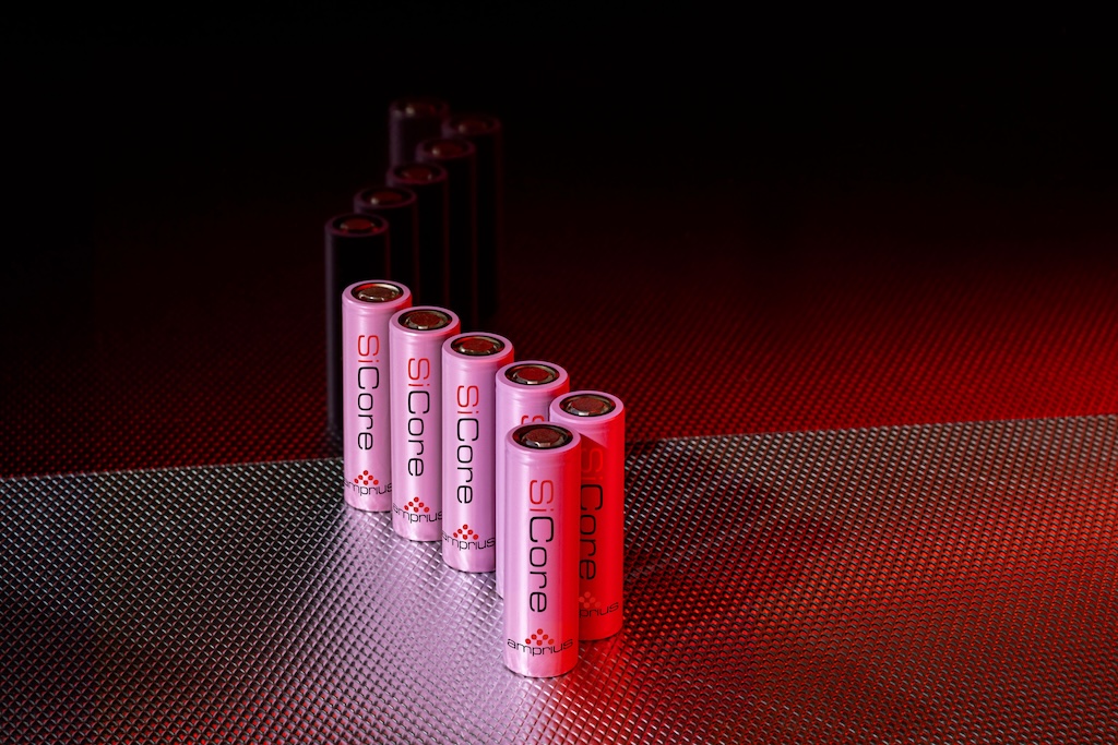 A series of pink and black cylindrical batteries arranged in a linear formation, set against a textured metallic background with subtle lighting.